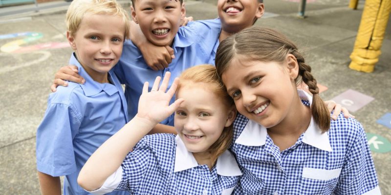 Two girls and three boys wearing school uniform smiling towards camera